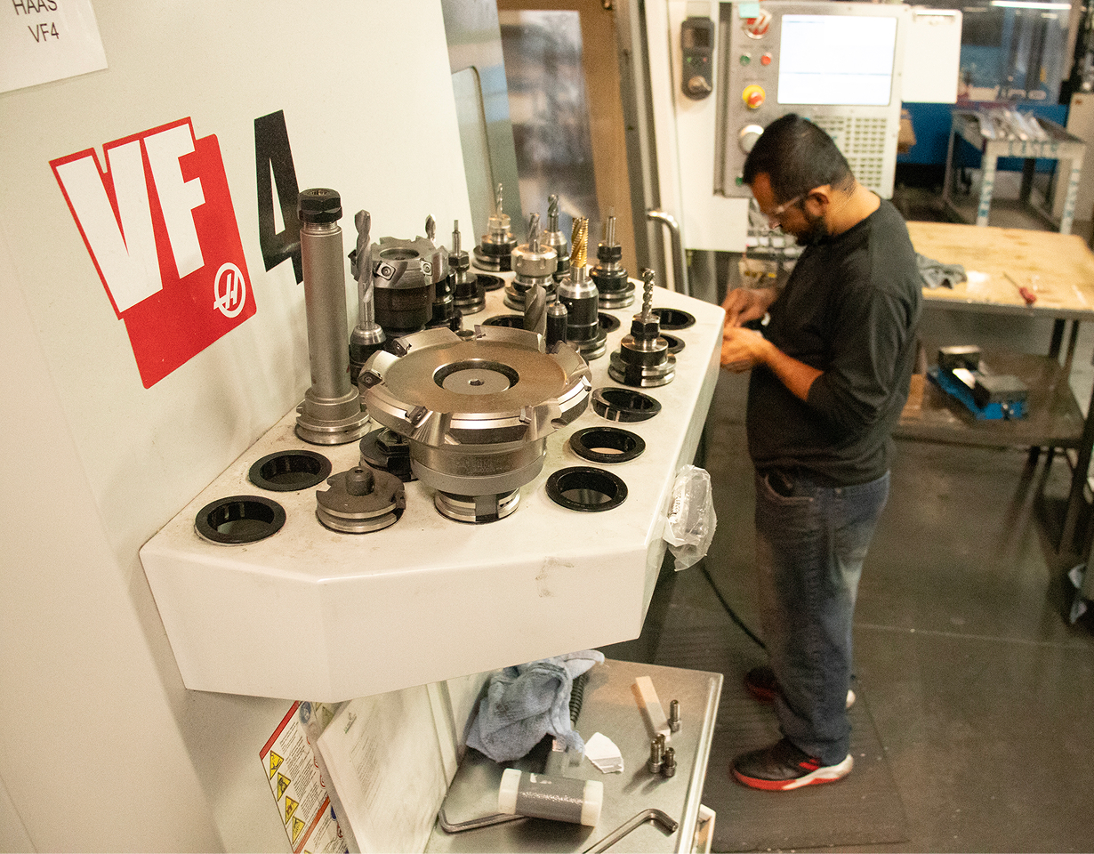 Machinist standing at a HAAS VF4 CNC mill, inspecting tooling laid out on the tool holder carousel.