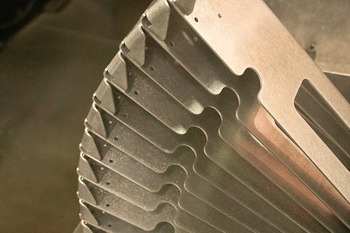 Stack of nested aluminum laser-cut brackets fanned in a curve, showing the precision edge profile from the cut.