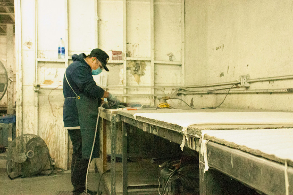 Worker grinding the surface of a long sheet stock workpiece in a finishing bay.
