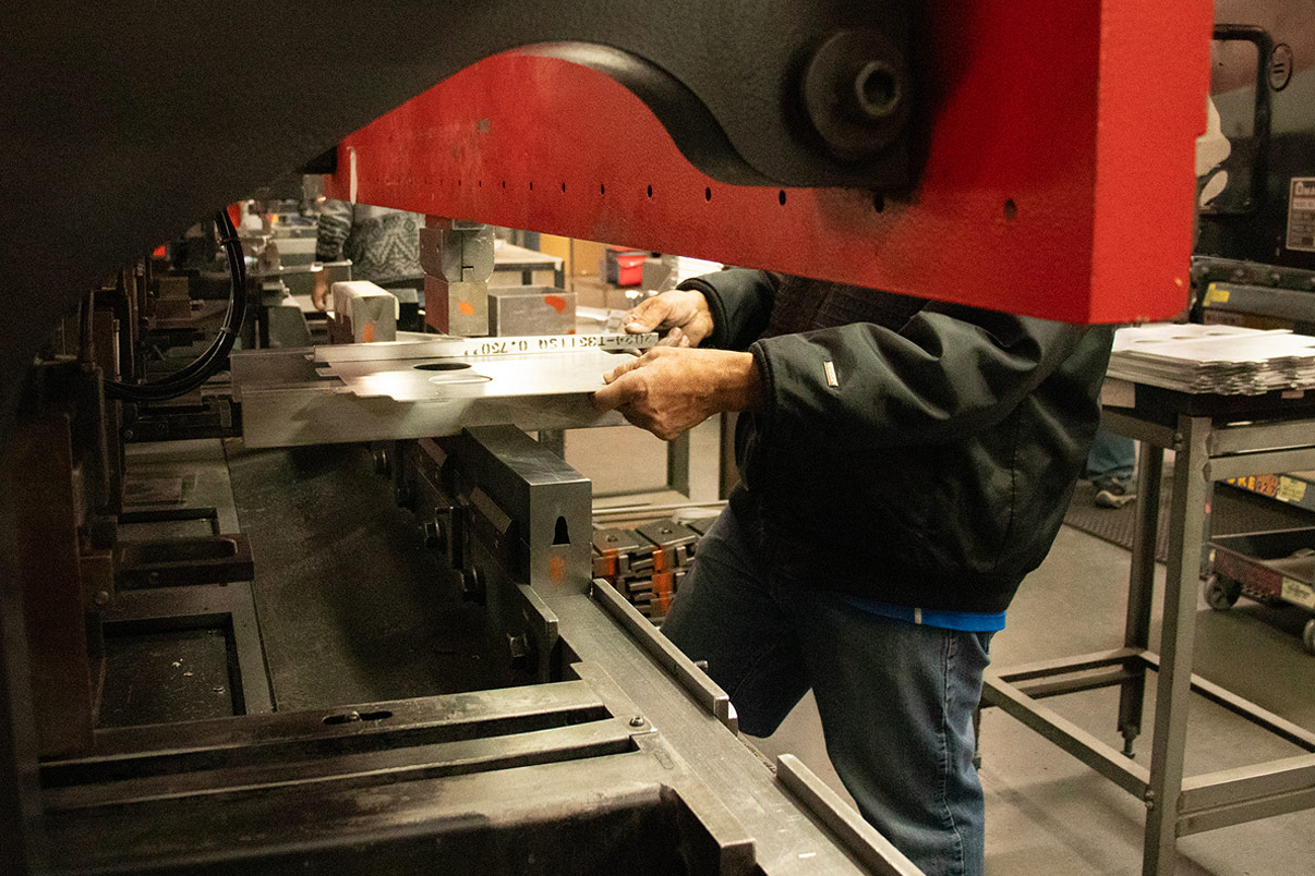 Operator at a press brake, feeding a punched sheet metal part into the dies for a bend operation.
